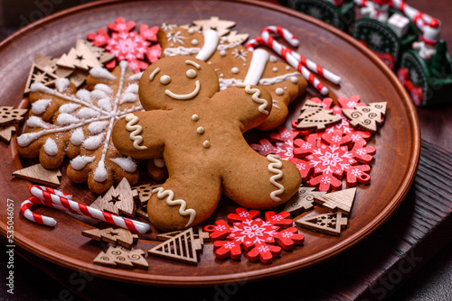 Beautiful gingerbread on a brown ceramic plate with Christmas tree decorations on a dark concrete background