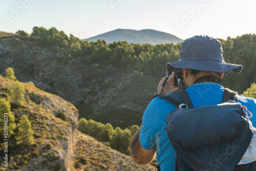 Rear view, hiker man with backpack taking photos at mountain landscape
