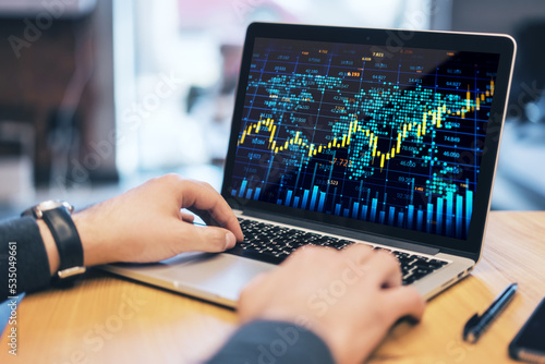 Close up of male hands at workplace with creative forex chart with candlestick graph, index and tech hologram on laptop screen, and supplies on office background. Trade, stock, and finance concept.