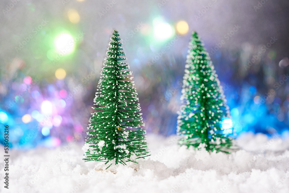 Christmas trees in the snow and christmas lights on blurred background.