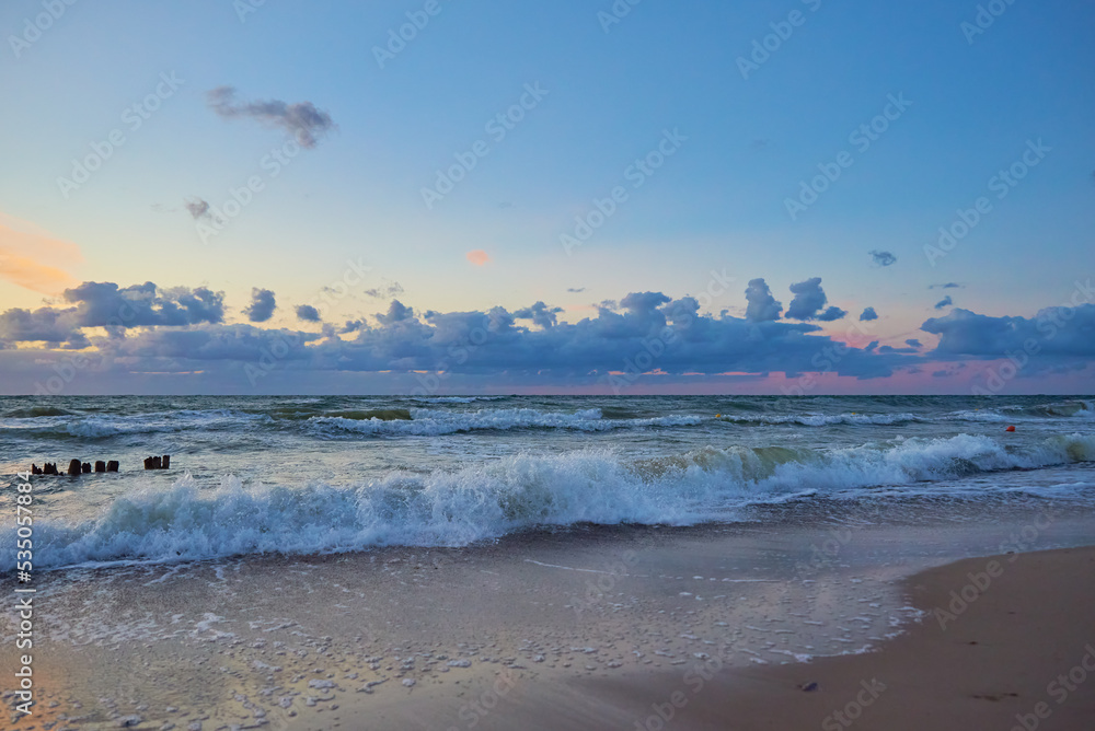 Panoramic view of sea beach with splashing waves against dramatic cloudy sky. Baltic sea coastline at sunset