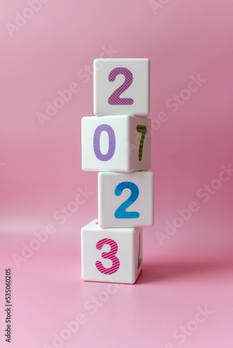 Cube tower with colorful numbers 2023 in center of the photo on pink background. New year, calendar.