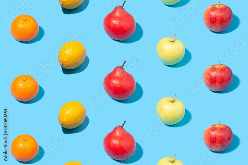 Ripe yellow apricots, apples, lemons and pears on light blue background - creative summer pattern