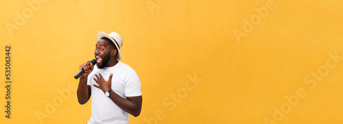 young handsome african american boy singing emotional with microphone isolated on yellow background, in motion gesturing