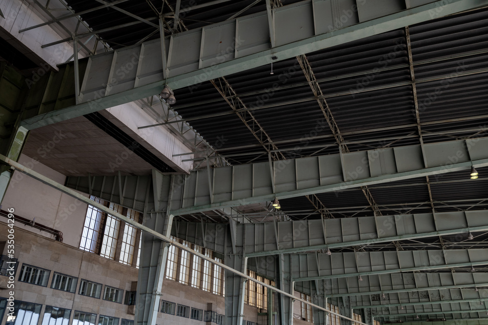 View under high ceiling of open interior space with huge steel truss, columns and beam structure building at former airport terminal in Berlin,  Germany.
