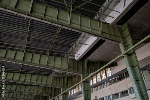 View under high ceiling of open interior space with huge steel truss, columns and beam structure building at former airport terminal in Berlin, Germany.