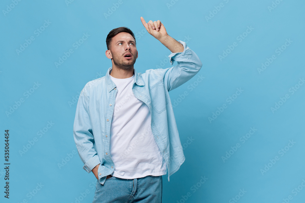 Thoughtful pensive tanned handsome man in casual basic t-shirt point finger up have good idea posing isolated on blue studio background. Copy space Banner Mockup. People emotions Lifestyle concept Thoughtful pensive tanned handsome man in casual basic t-shirt point finger up have good idea posing isolated on blue studio background. Copy space Banner Mockup. People emotions Lifestyle concept