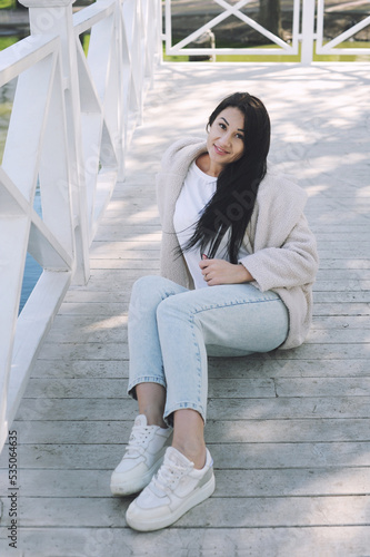 Happy young brunette woman outdoor, dressed in faux white fur coat and jeans