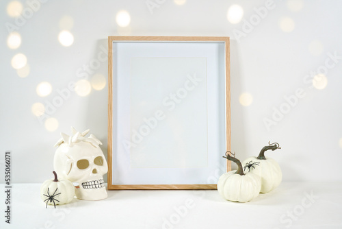 Halloween product mockup. Wall art picture frame mockup with white skull pumpkins against a white background with bokeh party lights. Negative copy space.