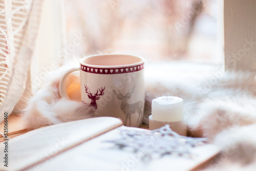 christmas still life. cup of cocoa, open book, white blanket, candle, handmade snowflake on windowstill near light window, selective focus photo