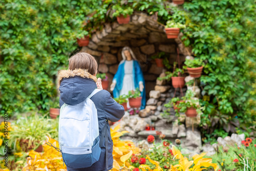 a boy stands in front of a statue of the Holy Virgin Mary and prays
