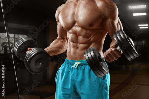 Muscular man working out in gym doing exercises with dumbbells. Strong male naked torso abs