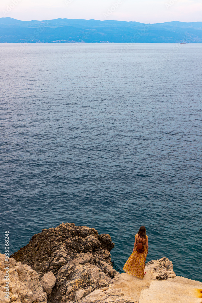 woman in a long elegant dress stands over paradise bay in croatia admiring the sunset, krk island, mediterranean sea, adriatic sea