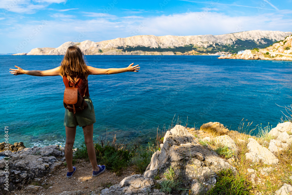 a beautiful girl stands over the rocky coast of croatia with her hands raised in the air; active vacation in croatia, hiking on the mediterranean sea, krk island a beautiful girl stands over the rocky coast of croatia with her hands raised in the air; active vacation in croatia, hiking on the mediterranean sea, krk island
