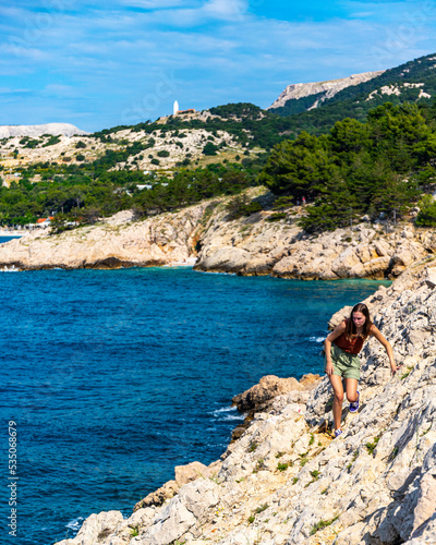 beautiful girl walks on the rocks on the shore of the adriatic enjoying the wonderful views in the background; vacation in croatia on krk island; hiking by vrzenica beach trail