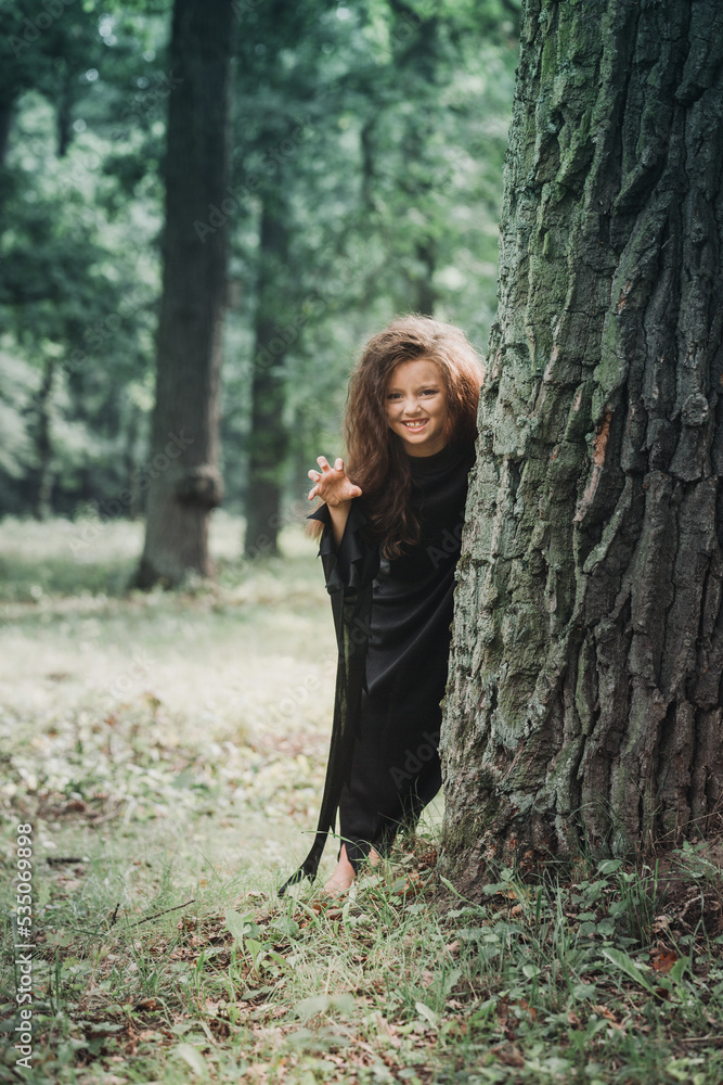 Little witch scares people from behind the tree, Halloween concept Little witch scares people from behind the tree, Halloween concept