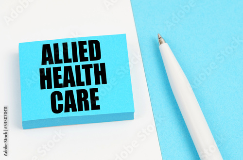 On a white and blue surface, a pen and blue stickers with the inscription - Allied Health Care