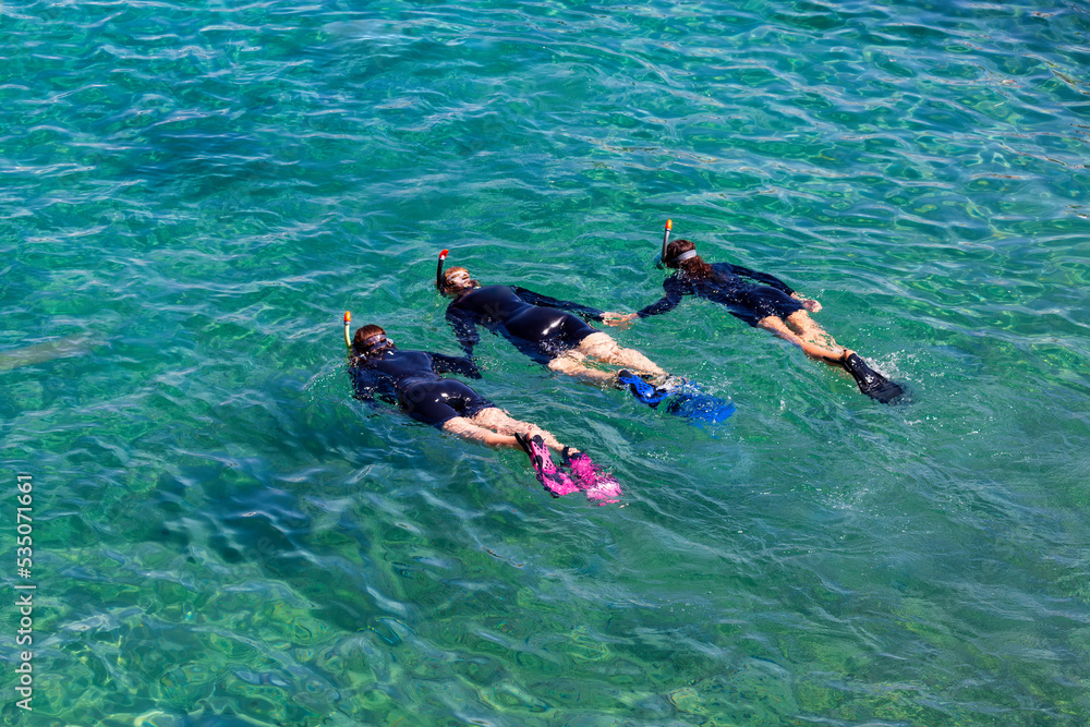 Three female divers with scuba masks and flippers diving in crystal clear water in Eilat, Red sea, Israel. Divers are training at the sea. Young girl diver in black scuba diving suits playing in water
