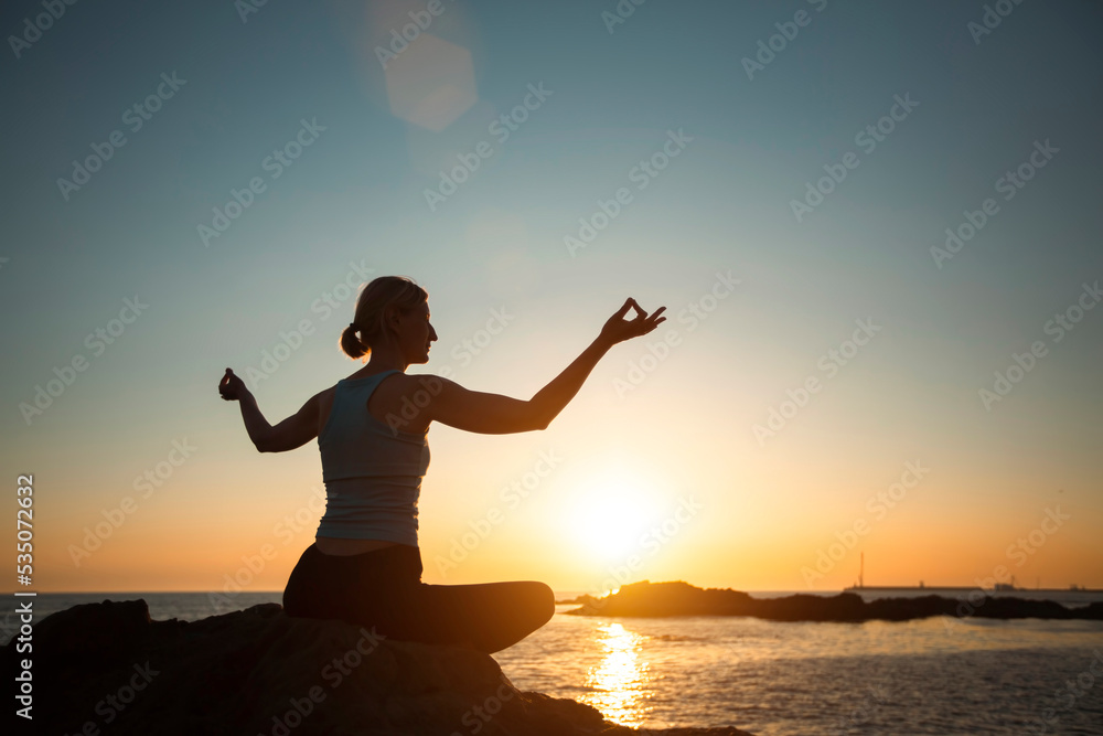 Yoga woman meditating in the lotus position during sunset on the oceanfront.