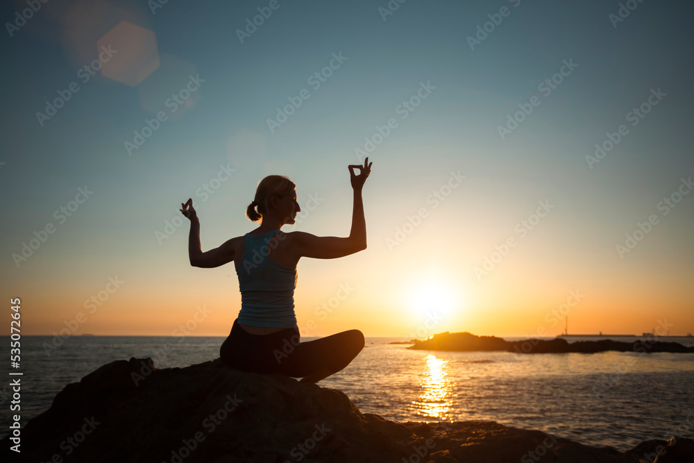 Silhouette of a woman practicing yoga during sunset on the ocean.