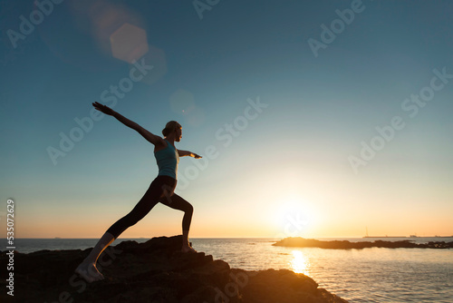 Silhouette of a woman doing gymnastic yoga into the sunset on the ocean.