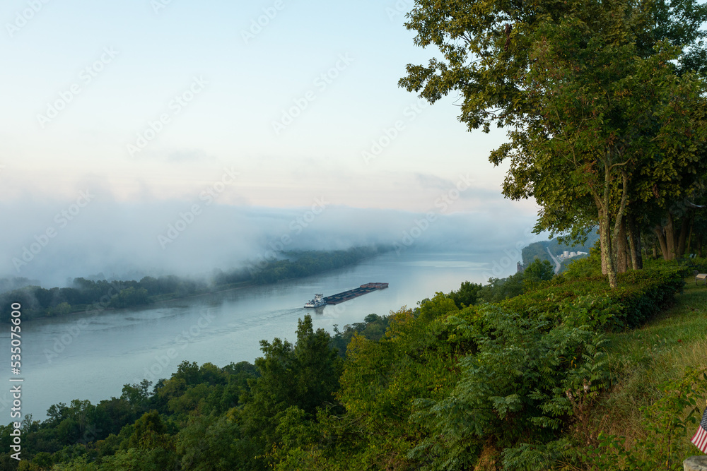 Barge floating down foggy Ohio river valley. 