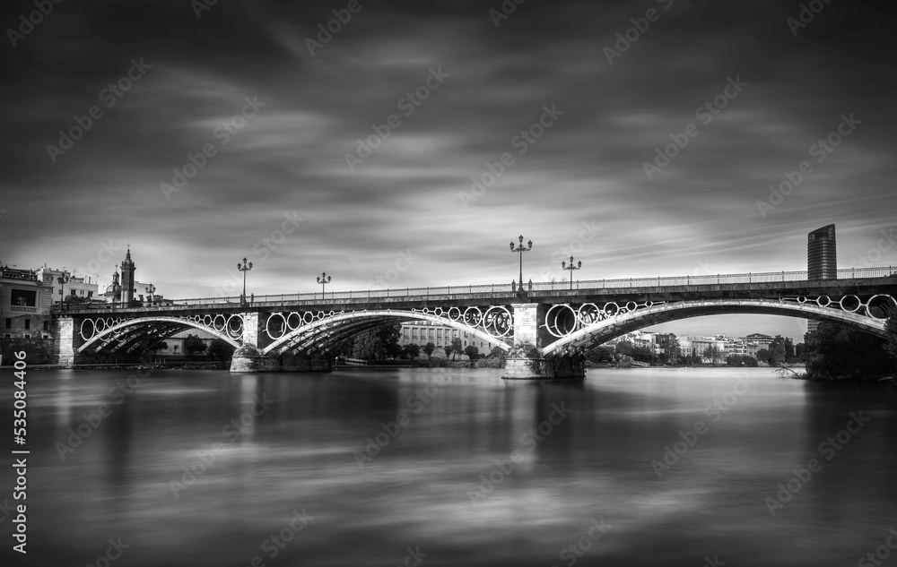 Triana bridgeSeville’s most popular bridge made from iron and moving clouds on sky long exposure photo with black and white edit