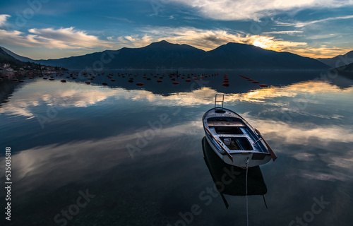 Kotor bay with beautiful reflections on water and fishing boats mountaind and colorful sky photo