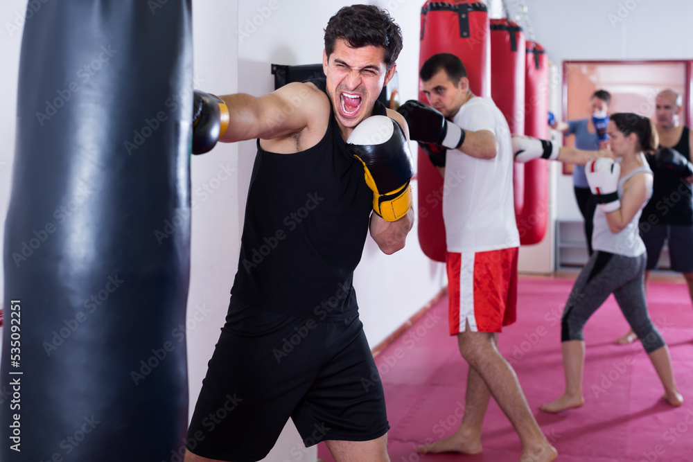 enthusiastic sportsman in the boxing hall practicing boxing punches with boxing bag during training