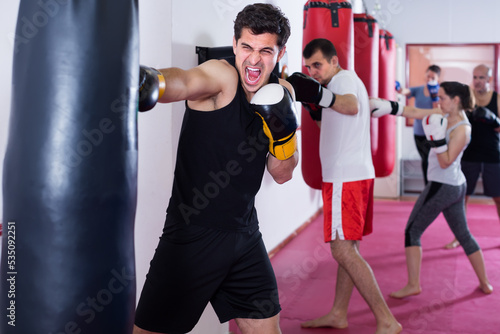 enthusiastic sportsman in the boxing hall practicing boxing punches with boxing bag during training © JackF