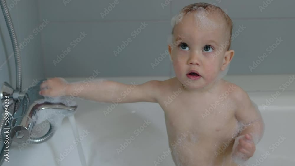 little naked baby child standing in bath tube filling hot water soap