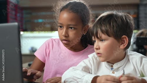 Multiethnic elementary school children working together on school project using laptop in class. Focused african girl and caucasian boy learning together in a modern school. 