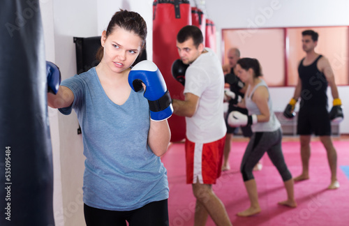 Female boxer is beating a boxing bag in the boxing hall. © JackF