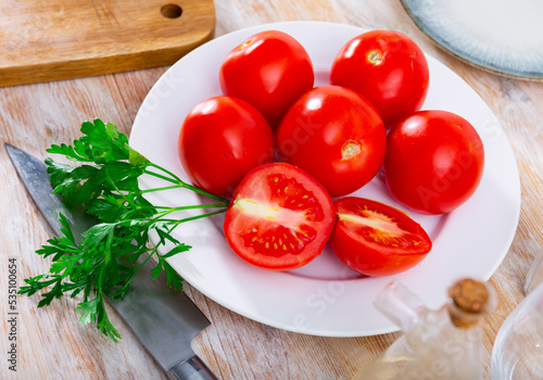 Fresh red tomatoes on wooden table with kitchen knife and bunch of parsley.