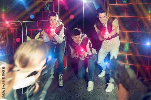 Joyful people aiming laser guns at other players during lasertag game in dark room