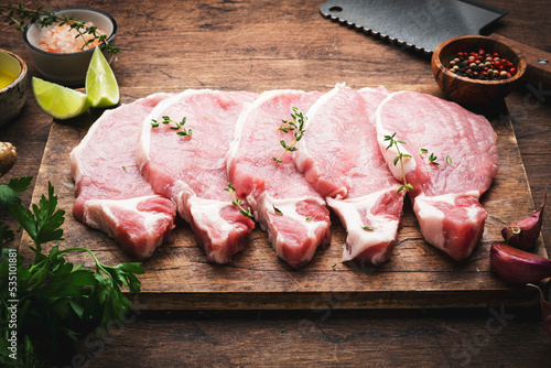 Fotomural Raw pork chops, meat on rustic wooden cutting board prepared for cooking with garlic, thyme, spices and pepper