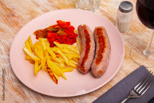 Appetizing grilled sausages served with fried potato and sliced red pepper