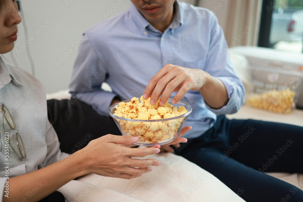 Close up hand of A couple pick popcorn to eat , Young couple relaxation at home watching a movie and eating popcorn, enjoy and happy living at home concept