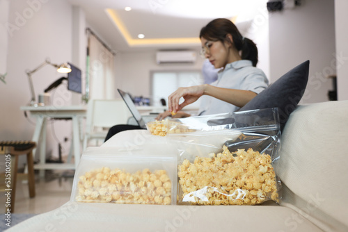 Young women eat popcorn while working on Sofa at home, work at home lifestyle