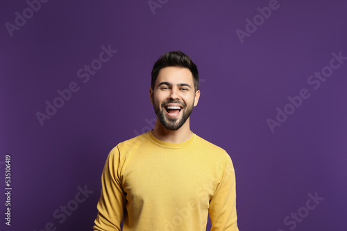 Young man laughing on purple background. Funny joke