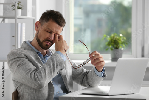 Man suffering from eyestrain at desk in office photo