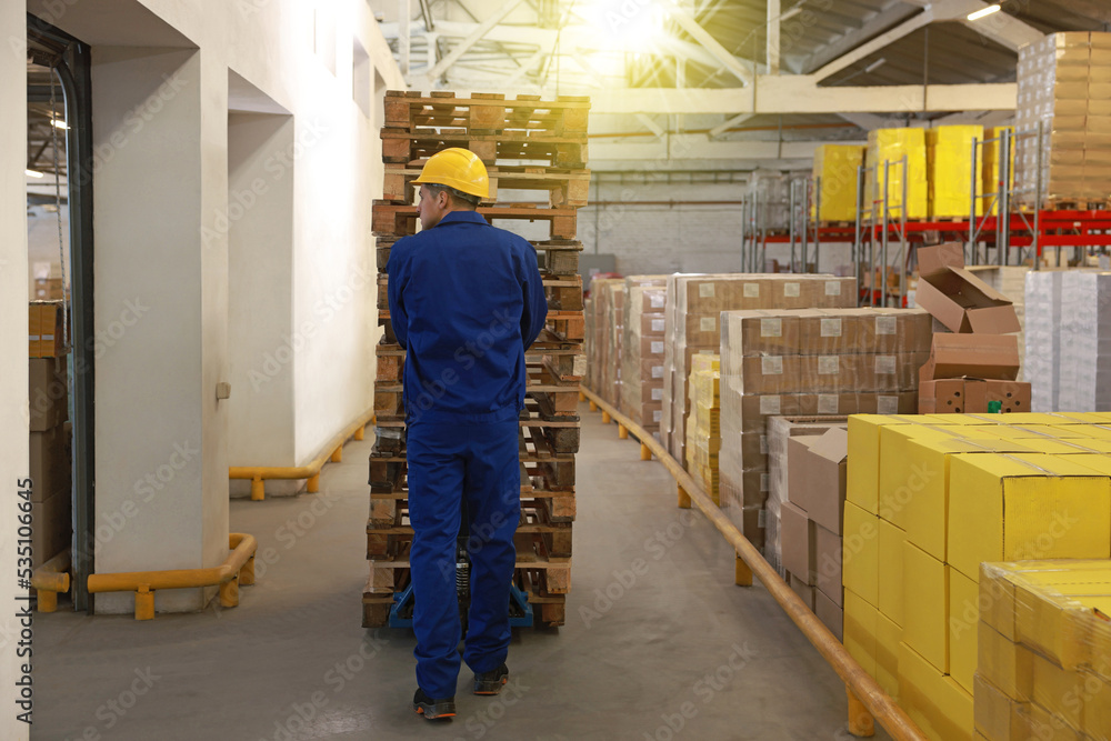 Worker moving wooden pallets with manual forklift in warehouse, back view Worker moving wooden pallets with manual forklift in warehouse, back view