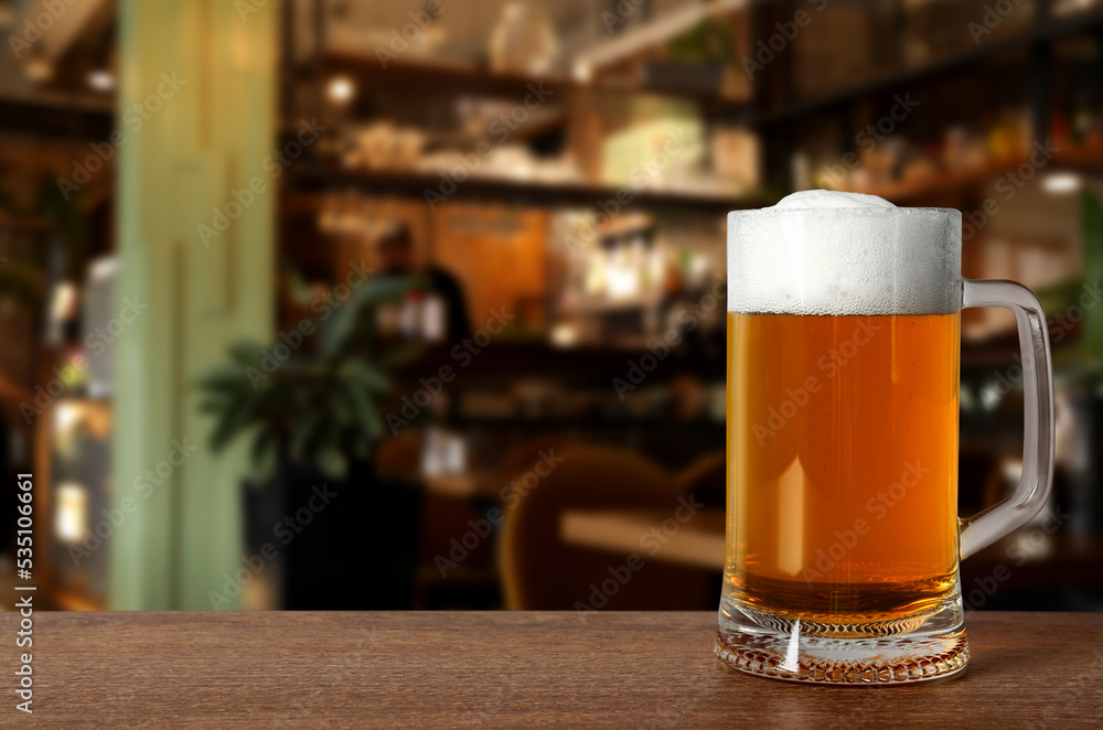 Glass mug with cold tasty beer on wooden table in pub, space for text Glass mug with cold tasty beer on wooden table in pub, space for text