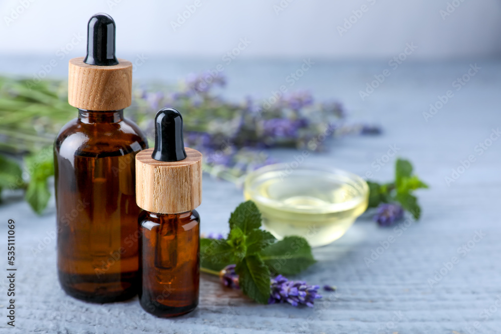 Bottles of essential oil, mint and fresh lavender on grey wooden table, space for text