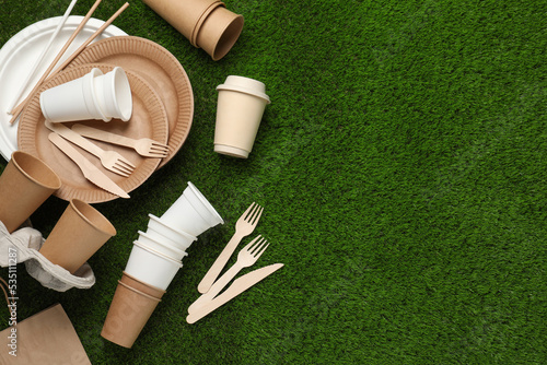Eco disposable tableware on green artificial grass, flat lay. Space for text photo