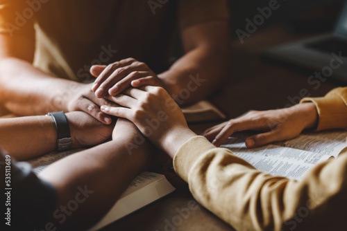 Christian group of people holding hands praying worship together to believe and Bible on a wooden table for devotional for prayer meeting concept.