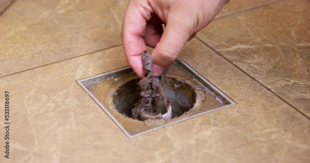 Hand pulls bun of female dirty hair from drain hole in bathroom. DIY