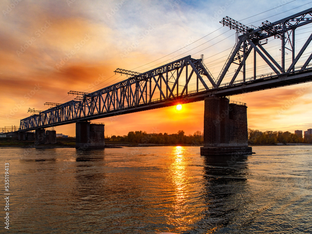 First railway metal bridge over the great Siberian river Ob in Novosibirsk, stone pillars in the water, copy space, place for text, sunset sky