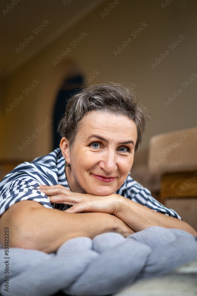 Obraz premium Portrait smiling middle aged gray haired woman posing with hands near chin lying on gray plaid floor