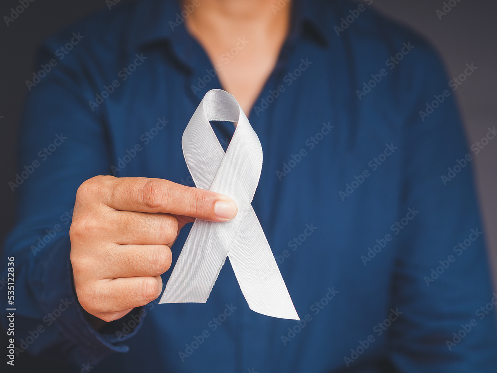Close-up of hand holding a white ribbon on a gray background - obrazy, fototapety, plakaty 